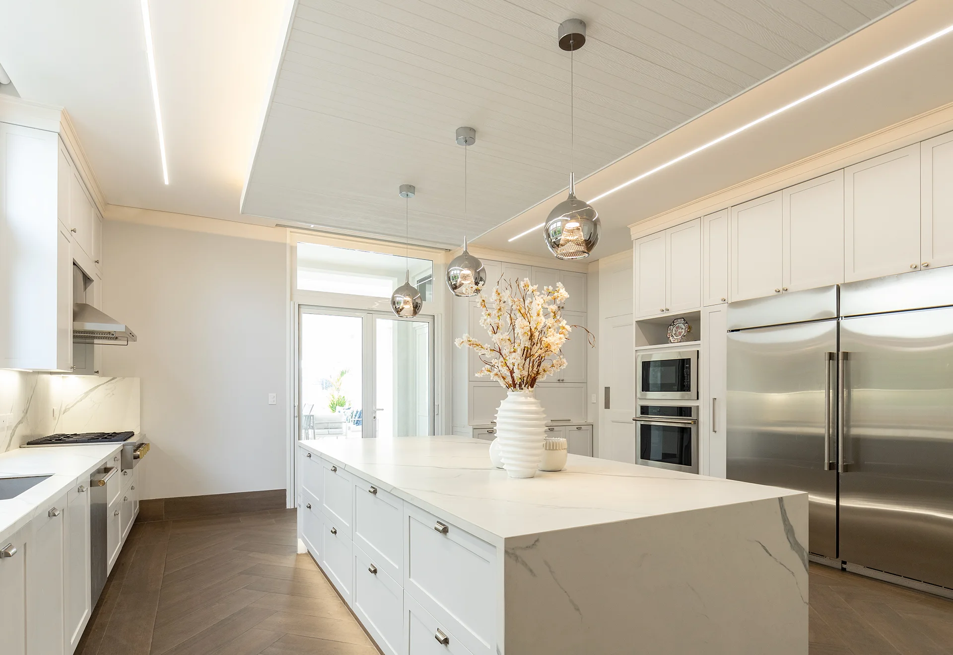 Cocina blanca con isla central e iluminación lineal